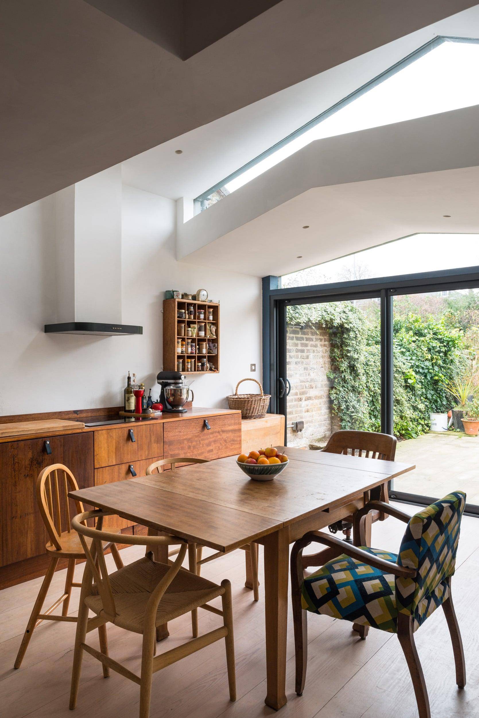 Interior view of a dining area with wooden furniture, a large sliding glass door opening to greenery, and a skylight; architecture by Gresford Architects.