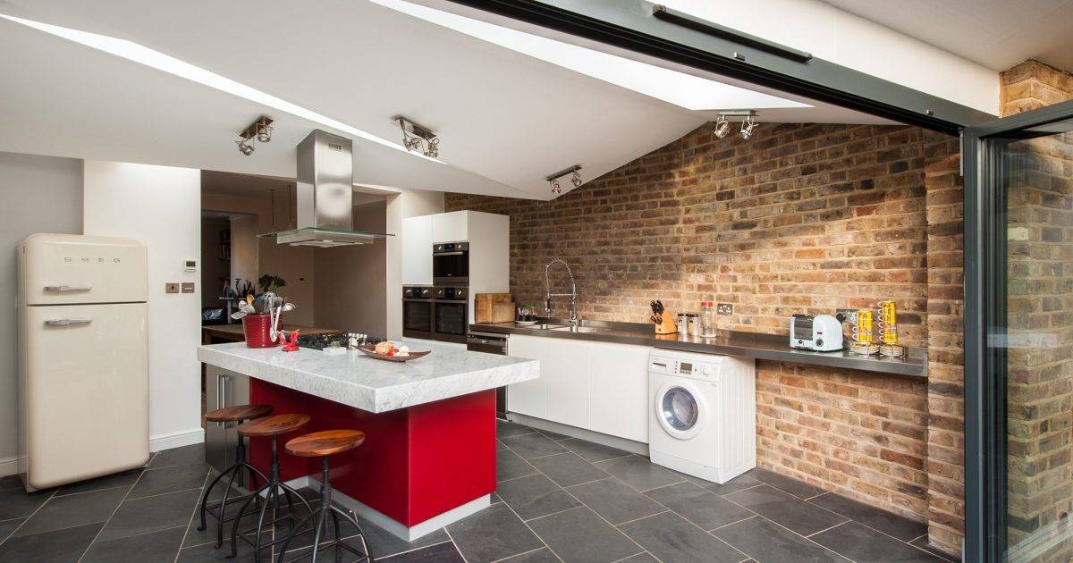 Gresford Architects Ltd — Modern kitchen with brick wall, white cabinetry, red island, and black tiled flooring, architecture by Gresford Architects.
