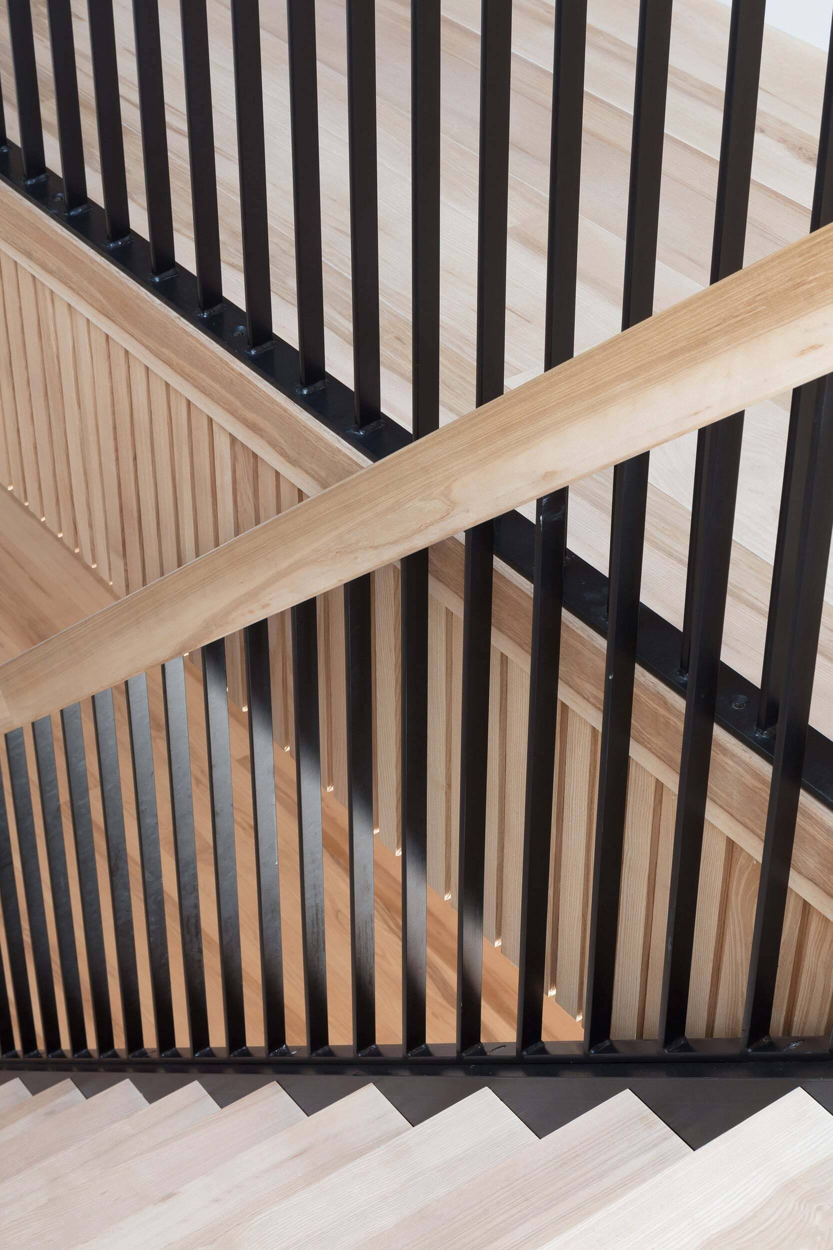 Interior staircase with black metal railing, wooden handrail, and wooden wall panels, architectural detail by Gresford Architects.