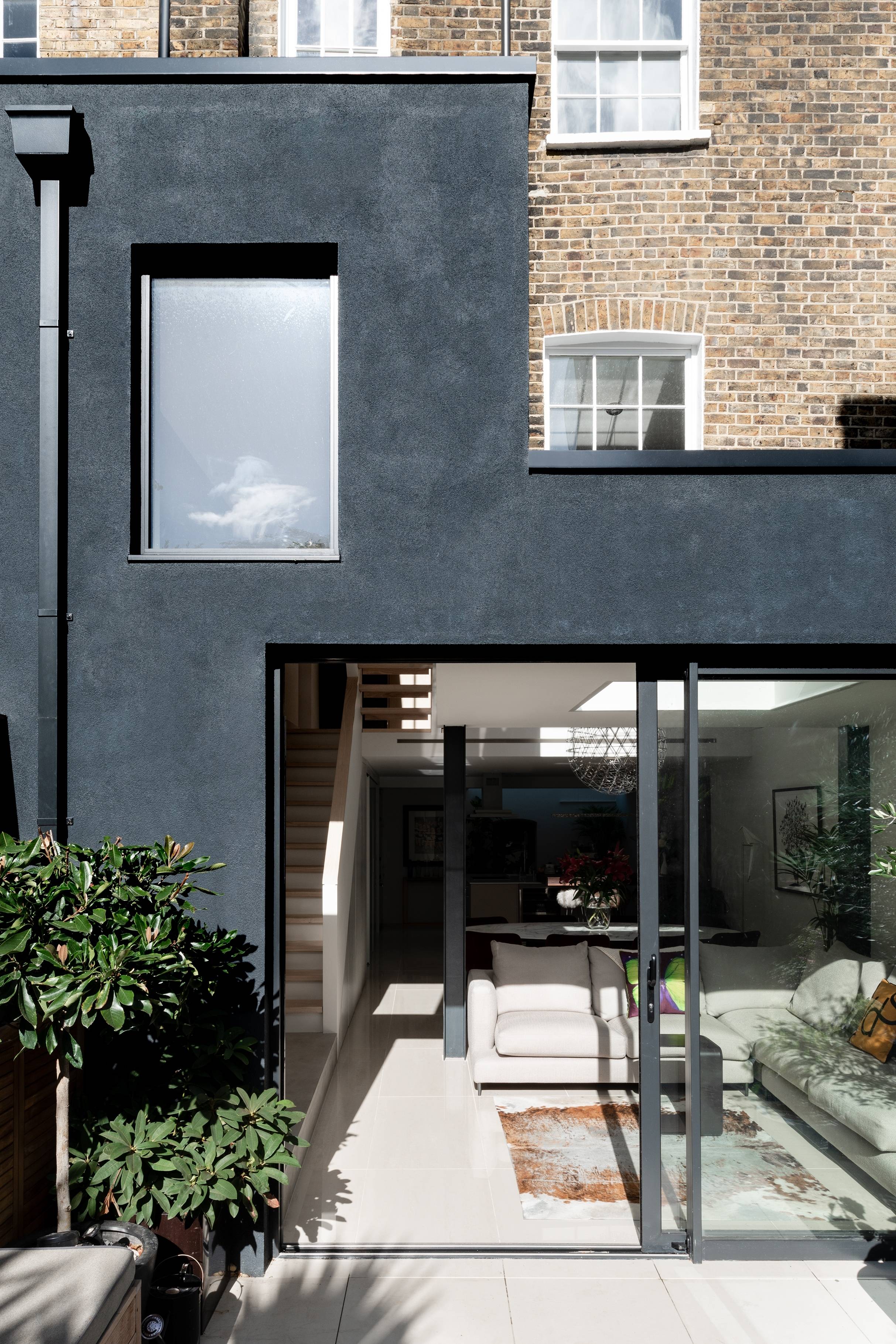 Modern grey extension with large glass doors revealing a bright interior, brick building backdrop, greenery, and architecture by Gresford Architects.