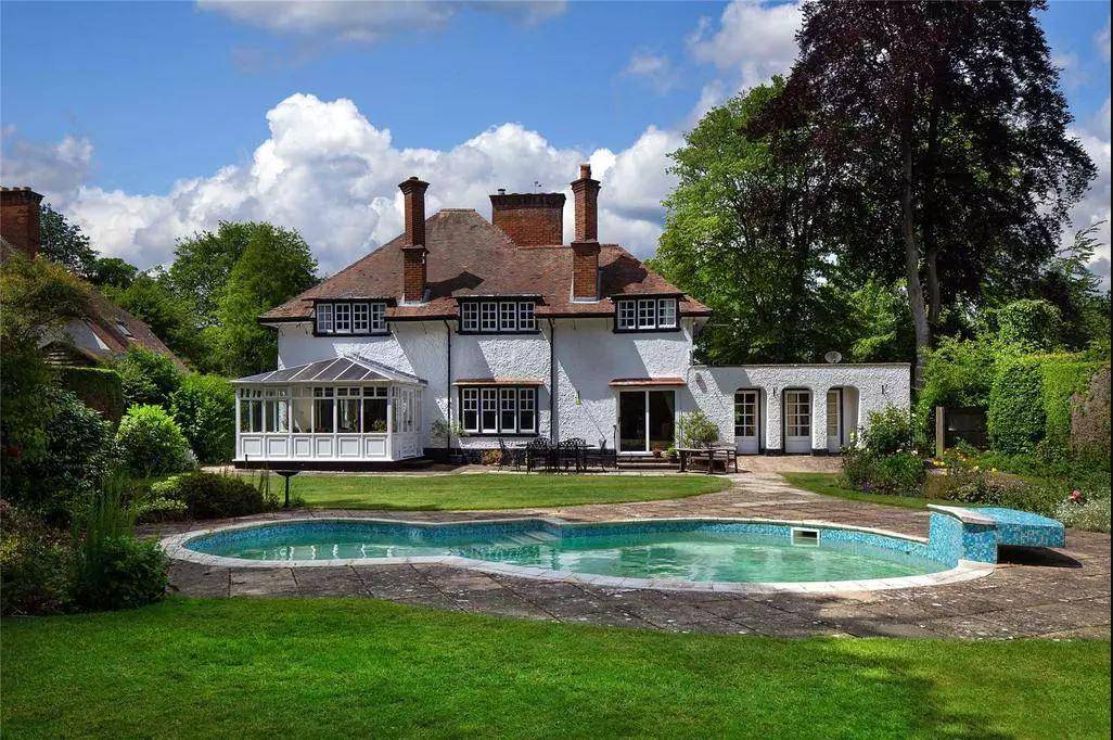 A large white house with multiple chimneys, surrounded by lush trees, with a swimming pool in the foreground and a garden, architecture by Gresford Architects.