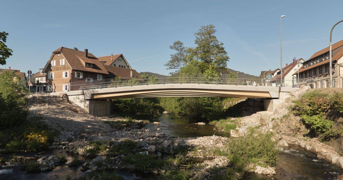 Moxon Architects Ltd — Modern concrete bridge over a small stream in a residential area with trees and houses, architecture by MOXON Architects.