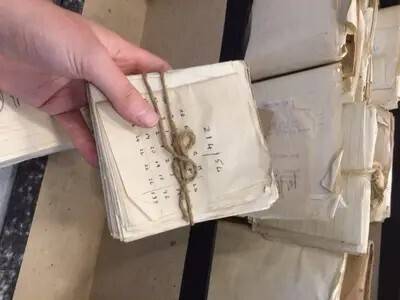 A hand holds a bundle of handwritten notes tied with twine, with more bundles on a desk. image from the Tavistock Institute of Human Relations website.
